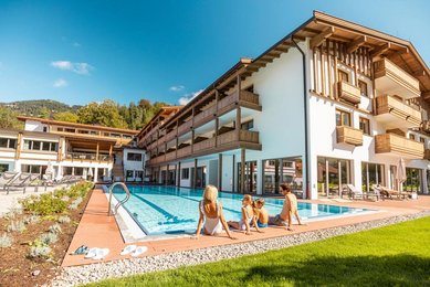 Mutter sitzt mit ihren beiden Kindern in Badekleidung am Beckenrand des Außenpools im Familienhotel Das Bayrischzell.