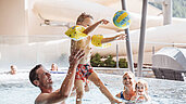 Mutter und Vater planschen gemeinsam mit ihren beiden Kindern im Familienschwimmbad im Familienhotel Huber.