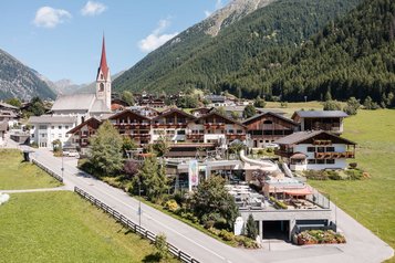 Das Familienhotel Huber von außen im Sommer. Auf dem Hotelgelände befindet sich ein Außenpool.
