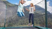 Zwei Mädchen springen auf dem Trampolin draußen auf dem Außengelände des Kinderhotels Sailer in Tirol.
