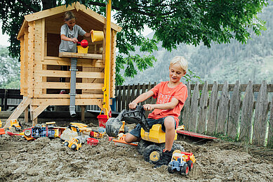 Zwei Kinder spielen im großen Sandkasten auf der Abenteuerwiese des Kinderhotels Sailer in Tirol.