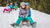 Jugendliche fahren auf dem Schlitten einen Berg im Salzburger Land hinab.
