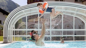 Vater planscht mit seinem Kind im Außenpool des Familienhotels Kaiserhof in Tirol.