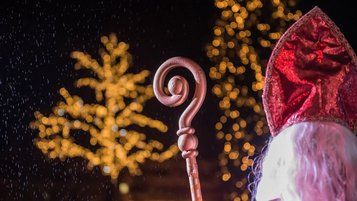 Nikolaus in rotem Gewand mit Bischofsstab steht vor leuchtenden Weihnachtsbäumen bei einer stimmungsvollen Feier im Familienhotel
