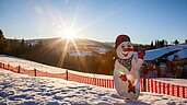 Ein hölzerner Schneemann steht auf einer Skipiste im familienfreundlichen Skigebiet in der Steiermark.