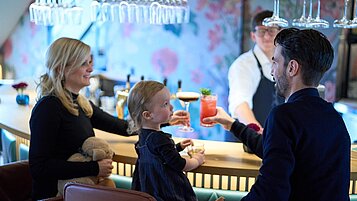 Eine Familie sitzt mit der Tochter an der Bar "Blindes Huhn" im Landhaus Averbeck und trinken einen Cocktail.