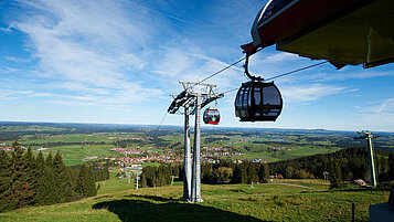Ausblick auf die Landschaft in Allgäu bei schönem Wetter. In der Szene fährt eine Gondel und bietet sich super an für einen Ausflug zum Erkunden.