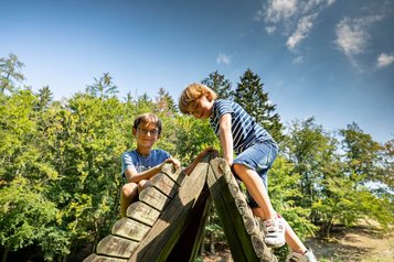 Zwei Kinder klettern auf einem Holzspielgerät im Garten des Familienhotel Ottonenhof.