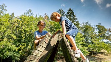 Zwei Kinder klettern auf einem Holzspielgerät im Garten des Familienhotel Ottonenhof.
