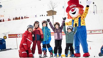 Einige Kinder bei einer Skischule jubeln mit dem Familotel-Maskottchen Happy