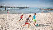 Drei Kinder spielen Fußball am Strand an der Ostsee.