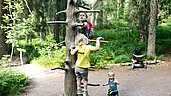 Kinder klettern an einem Kletterbaum im Wald.