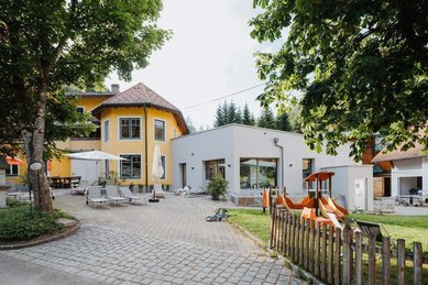 Der Außenbereich des Kinderhotels Bruckwirt in Oberösterreich mit Spielplatz ist vor dem Gebäude zu sehen.