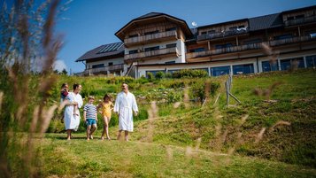 Familie genießt gemeinsame Wellnesszeit im Bademantel vor dem Familien Resort Petschnighof in Kärnten.