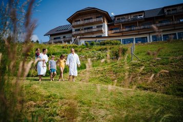 Familie genießt gemeinsame Wellnesszeit im Bademantel vor dem Familien Resort Petschnighof in Kärnten.