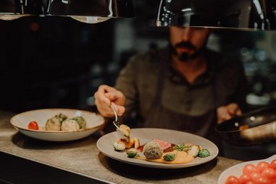 Familienhotel Mia Alpina in Tirol mit Koch beim Anrichten eines Gourmettellers in der Restaurantküche.