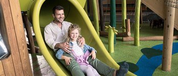 Vater und Tochter genießen eine fröhliche Rutschpartie im Indoor Spielbereich des Familienhotels mit natürlichem Design und viel Platz zum Toben