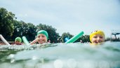 Kinder schwimmen im Schwimmbad mit Schwimmnudeln.