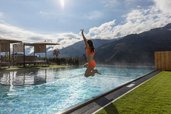 Mädchen springt fröhlich in den beheizten Außenpool des Familienhotels Almfamilyhotel Scherer mit Bergblick in Osttirol.