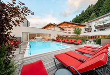 Außenpool mit roten Liegen und Bergkulisse im Familienhotel Amiamo im Salzburger Land.