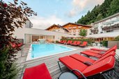 Außenpool mit roten Liegen und Bergkulisse im Familienhotel Amiamo im Salzburger Land.