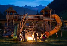 Kinder sitzen in einem Sitzkreis um ein Lagerfeuer mit einem Betreuer im Familienhotel Alphotel Tyrol Wellness & Family Resort in Südtirol.