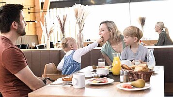 Familie sitzt mit den zwei Kindern am Frühstückstisch im Familienhotel. Alle Kinder werden immer All-Inclusive verpflegt.
