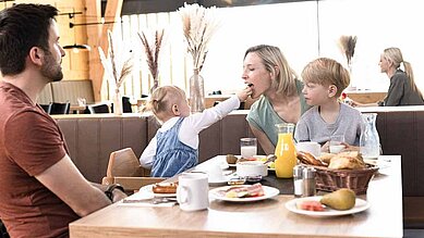 Familie sitzt mit den zwei Kindern am Frühstückstisch im Familienhotel. Alle Kinder werden immer All-Inclusive verpflegt.