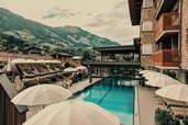 Poolbereich im Familienhotel Mia Alpina in Tirol mit Sonnenschirmen, Liegen und Bergpanorama.
