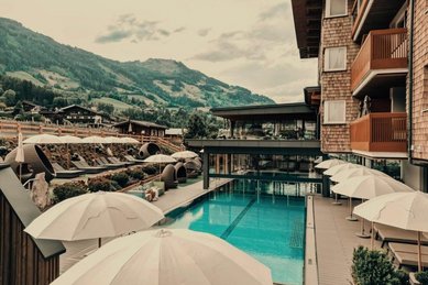 Poolbereich im Familienhotel Mia Alpina in Tirol mit Sonnenschirmen, Liegen und Bergpanorama.