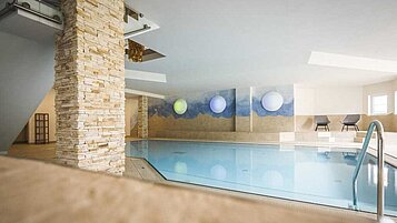 Familienfreundliches Hallenbad im Familienhotel Alpenhof im Allgäu mit klarem blauem Wasser und entspannendem Ambiente, betont durch eine Wandgestaltung mit Bergen und sanftem Licht.