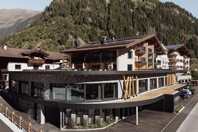 Sommeransicht des Familienhotels Kindl in den Tiroler Alpen mit umliegenden Wiesen, Bergen und traditioneller Architektur.