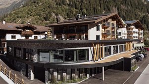 Sommeransicht des Familienhotels Kindl in den Tiroler Alpen mit umliegenden Wiesen, Bergen und traditioneller Architektur.