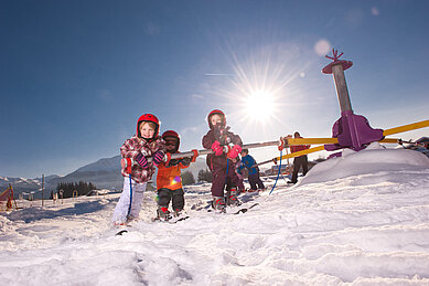 Drei kleine Mädchen stehen auf Skiern in Skiausrüstung am Übungslift des Familienhotels Landgut Furtherwirt in Tirol.