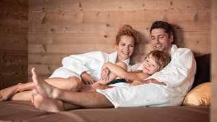 Familie mit Kind liegt gemütlich und entspannt im Bademantel auf einer Liege im Wellnessbereich des Hotels Family Home Alpenhof.