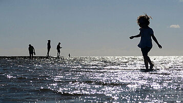 Mädchen läuft barfuß durch das flache Wasser am Strand an der Nordsee.