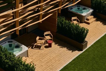 Terrasse im Familienhotel Bella Vista in Südtirol mit Whirlpool, Liegen, Holzboden und privatem Gartenbereich.