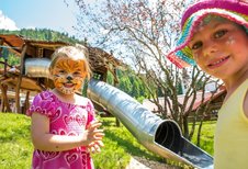 Zwei Mädchen sind im Gesicht bemalt und stehen vor einer Rutsche auf dem Spielplatz des Familienhotel Spa- & Familien-Resorts Krone im Allgäu ausklingen.