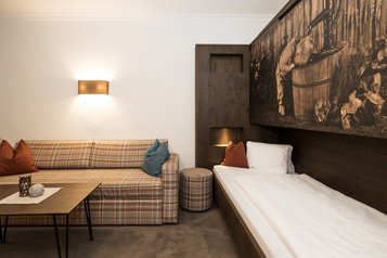 Kinderfreundlicher Schlafbereich im Familienhotel Oberkarteis mit gemütlichem Einzelbett, Sofa und liebevoller Holzeinrichtung.