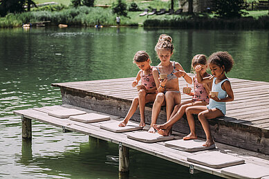 Kinder sitzen am See auf dem Steg im Familienhotel Post Family Resort im Salzburger Land.