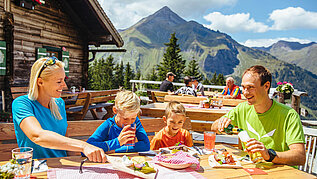 Familie sitzt im Biergarten auf einer Hütte im Salzburger Land und genießt regionale Spezialitäten.