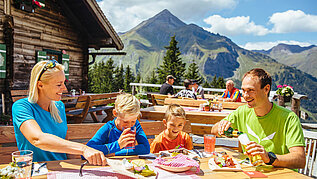 Familie sitzt im Biergarten auf einer Hütte im Salzburger Land und genießt regionale Spezialitäten.