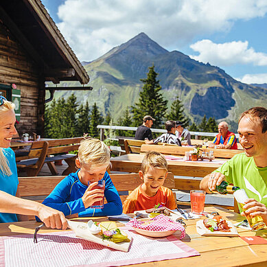 Familie sitzt im Biergarten auf einer Hütte im Salzburger Land und genießt regionale Spezialitäten.