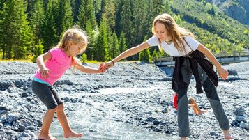 Mama und ihre Tochter gehen über Steine und eine Bach.