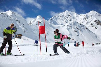 Kind fährt beim Skirennen durch einen Slalomkurs im Gäste-Winterprogramm des Hotels Bella Vista in Südtirol, im Hintergrund schneebedeckte Berge.