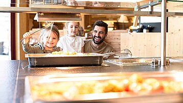 Vater mit zwei Töchtern am Kinderbuffet, Tochter nimmt sich Spaghetti zum Essen.