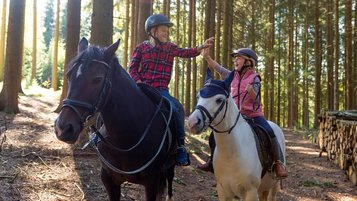 Zwei Kinder reiten durch die Waldlandschaft rund um das Familienhotel Ulrichshof im Bayerischen Wald