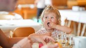 Kleines Kind isst fröhlich beim Frühstück im Restaurant des Familienhotel Sonne Bezau.