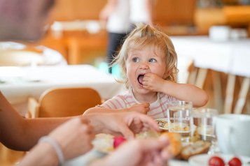 Kleines Kind isst fröhlich beim Frühstück im Restaurant des Familienhotel Sonne Bezau.