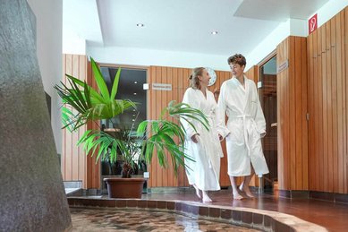 Zwei Jugendliche im Bademantel gehen lachend durch den Wellnessbereich des Familienhotel Sonne Bezau.